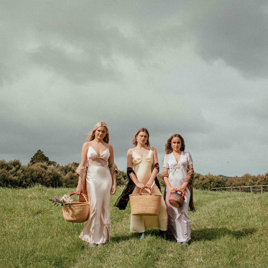 Three women walking together in a grassy field with a cloudy sky.