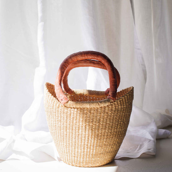 Woven basket with wooden handles on a white fabric background