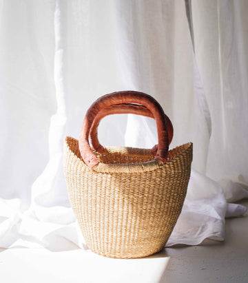 Woven basket with wooden handles on a white fabric background