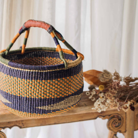 Woven basket with colorful handles on a wooden surface with a white curtain background