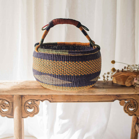 Woven basket with striped pattern on a wooden table against a white curtain background