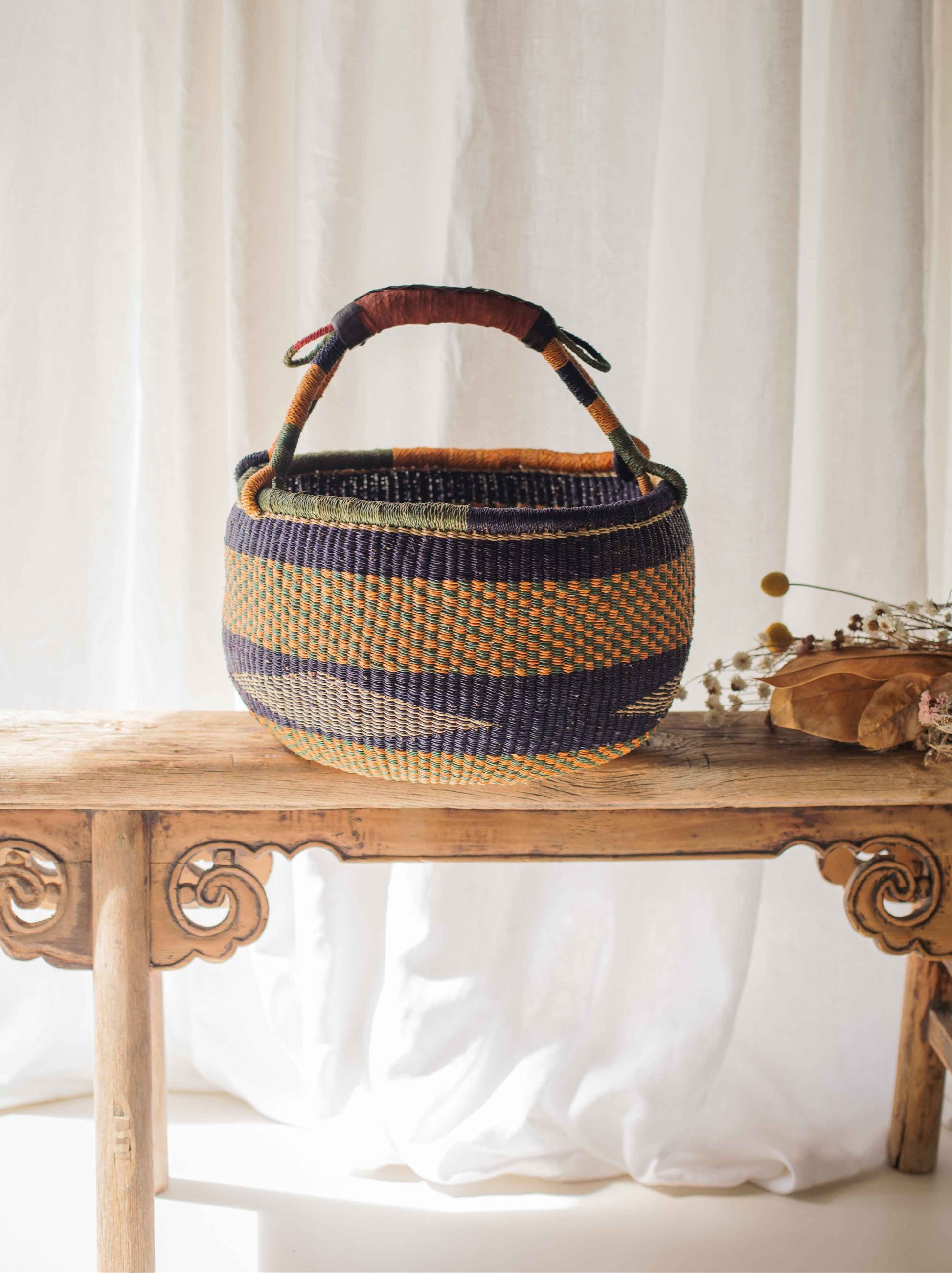 Woven basket with striped pattern on a wooden table against a white curtain background