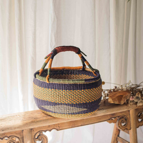 Woven basket with wooden handle on a wooden bench against a white curtain background