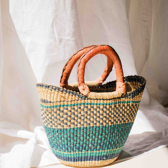 Woven basket with leather handle on a white fabric background