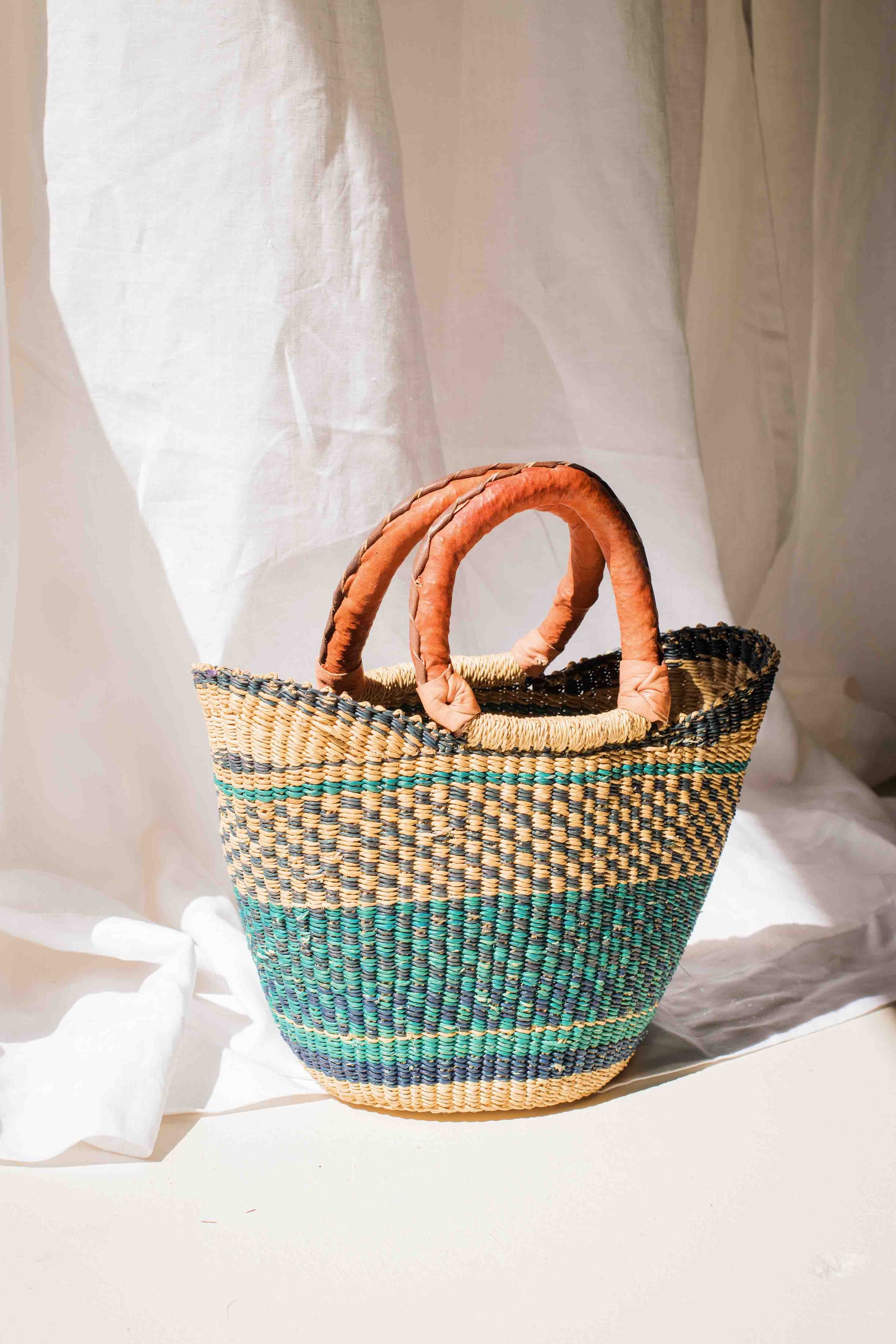 Woven basket with leather handle on a white fabric background