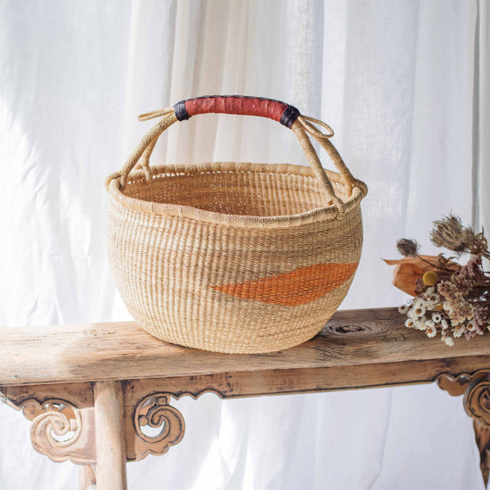Woven basket with a red and orange stripe on a wooden bench against a white curtain background