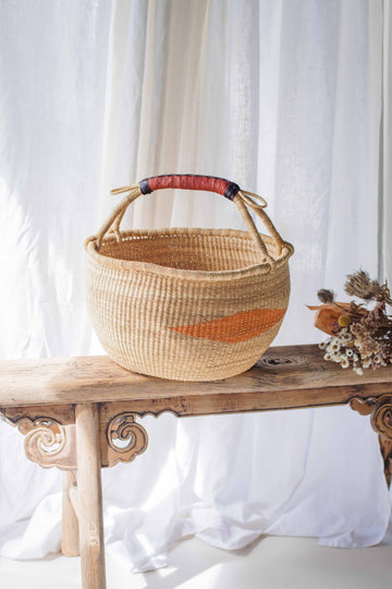 Woven basket with a red and orange stripe on a wooden bench against a white curtain background