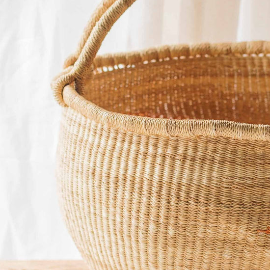 Woven basket with a wooden handle on a wooden table against a white curtain background