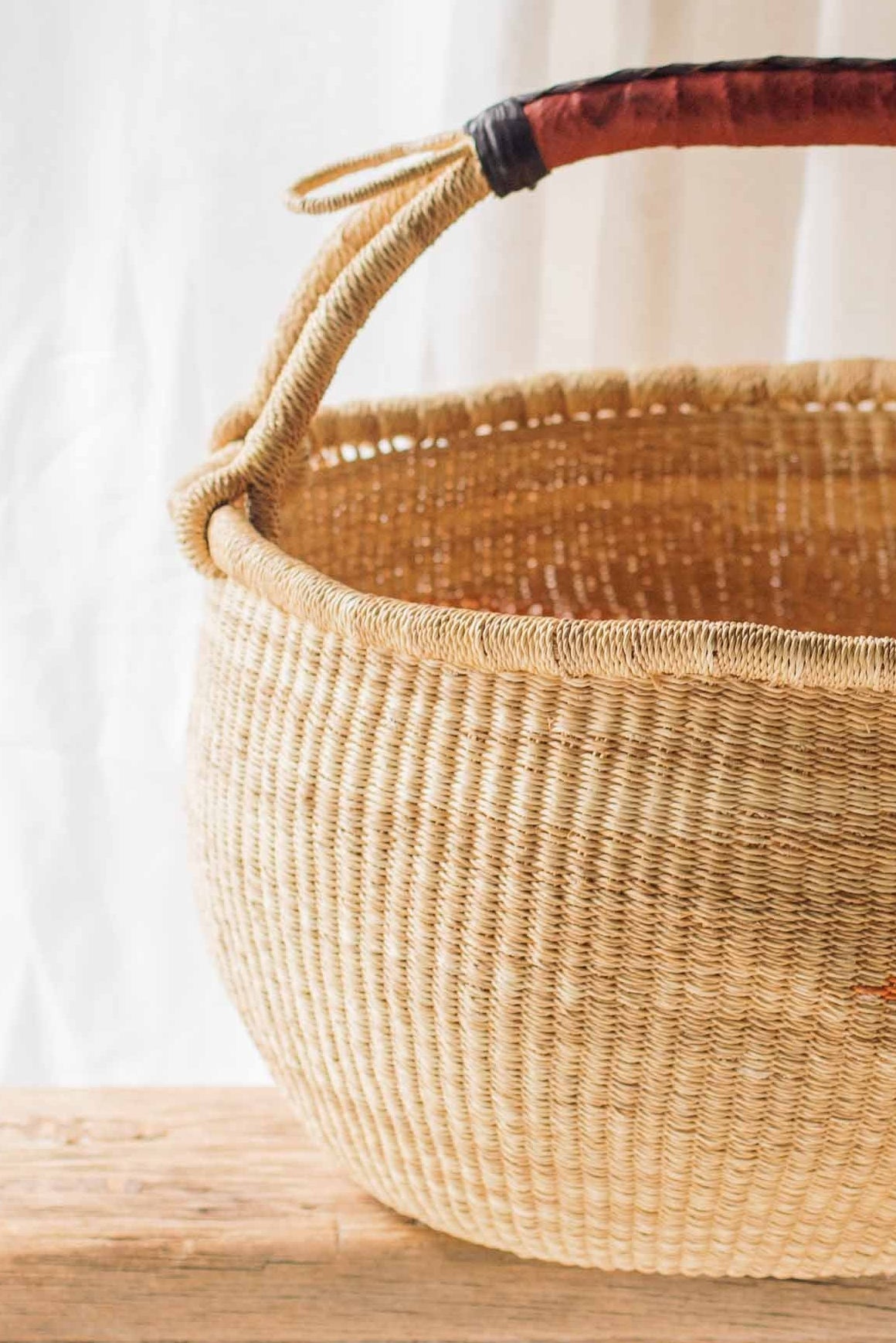 Woven basket with a wooden handle on a wooden table against a white curtain background