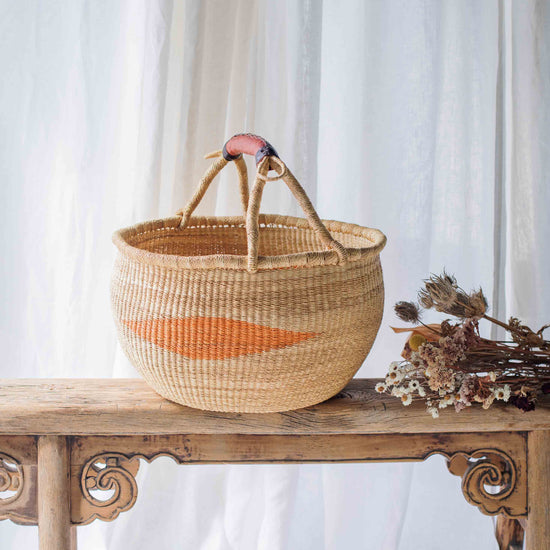 Woven basket with a pink handle on a wooden table with a white curtain background