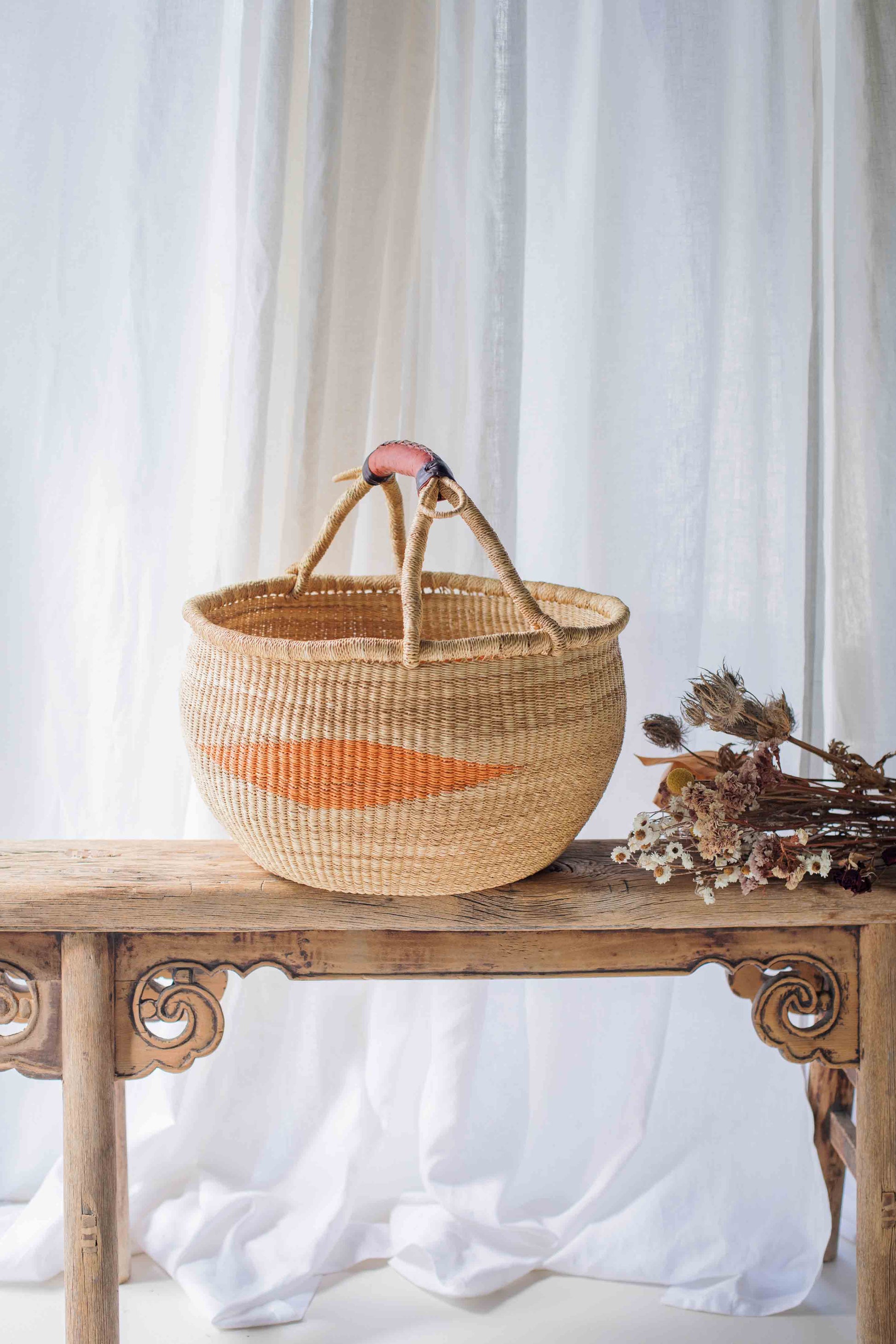 Woven basket with a pink handle on a wooden table with a white curtain background