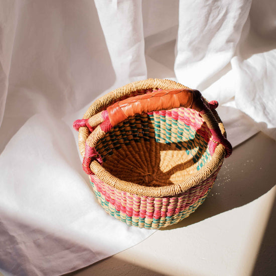 Woven basket with colorful handle on a white fabric background