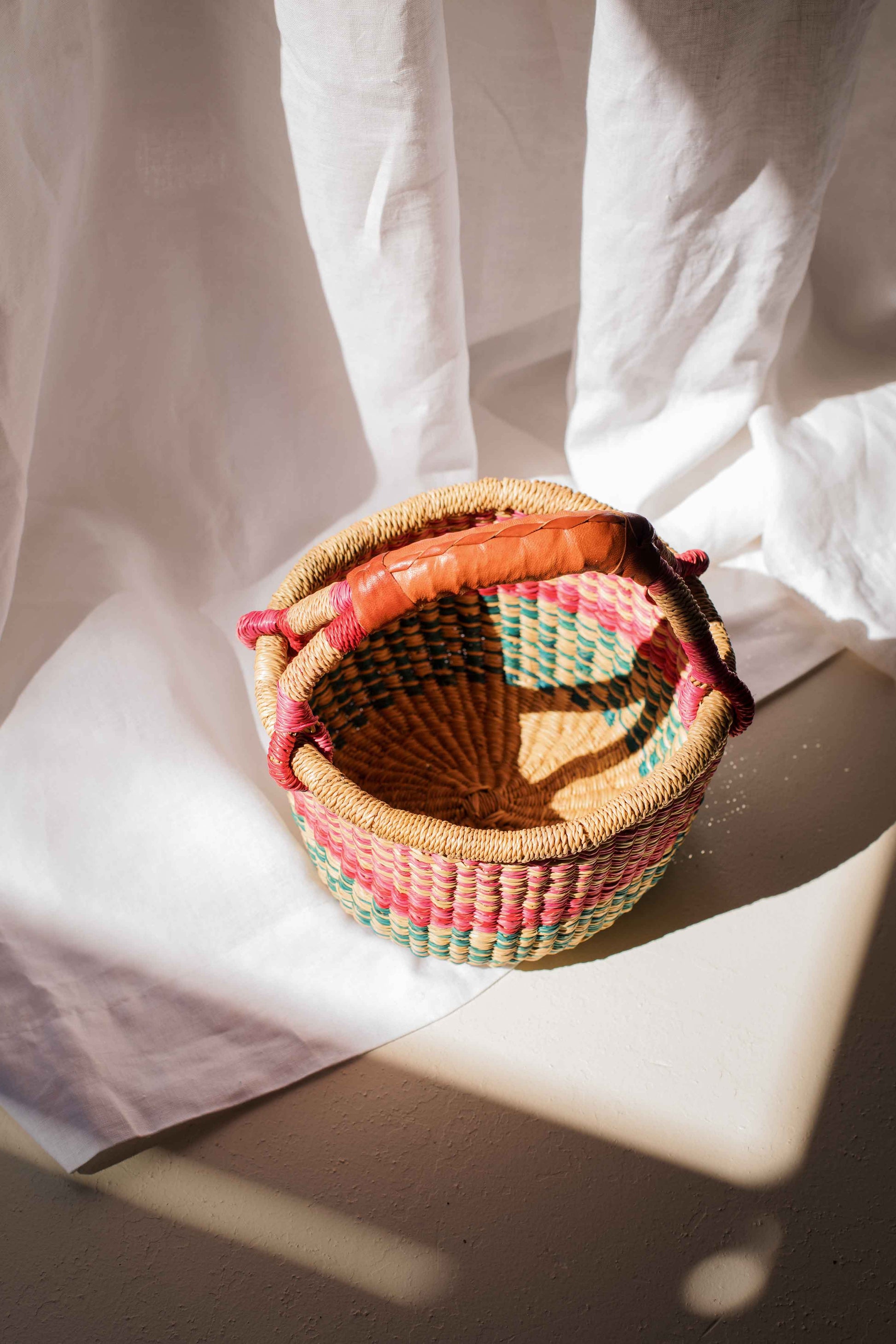 Woven basket with colorful handle on a white fabric background