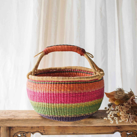 Colorful woven basket on a wooden table with a white curtain background