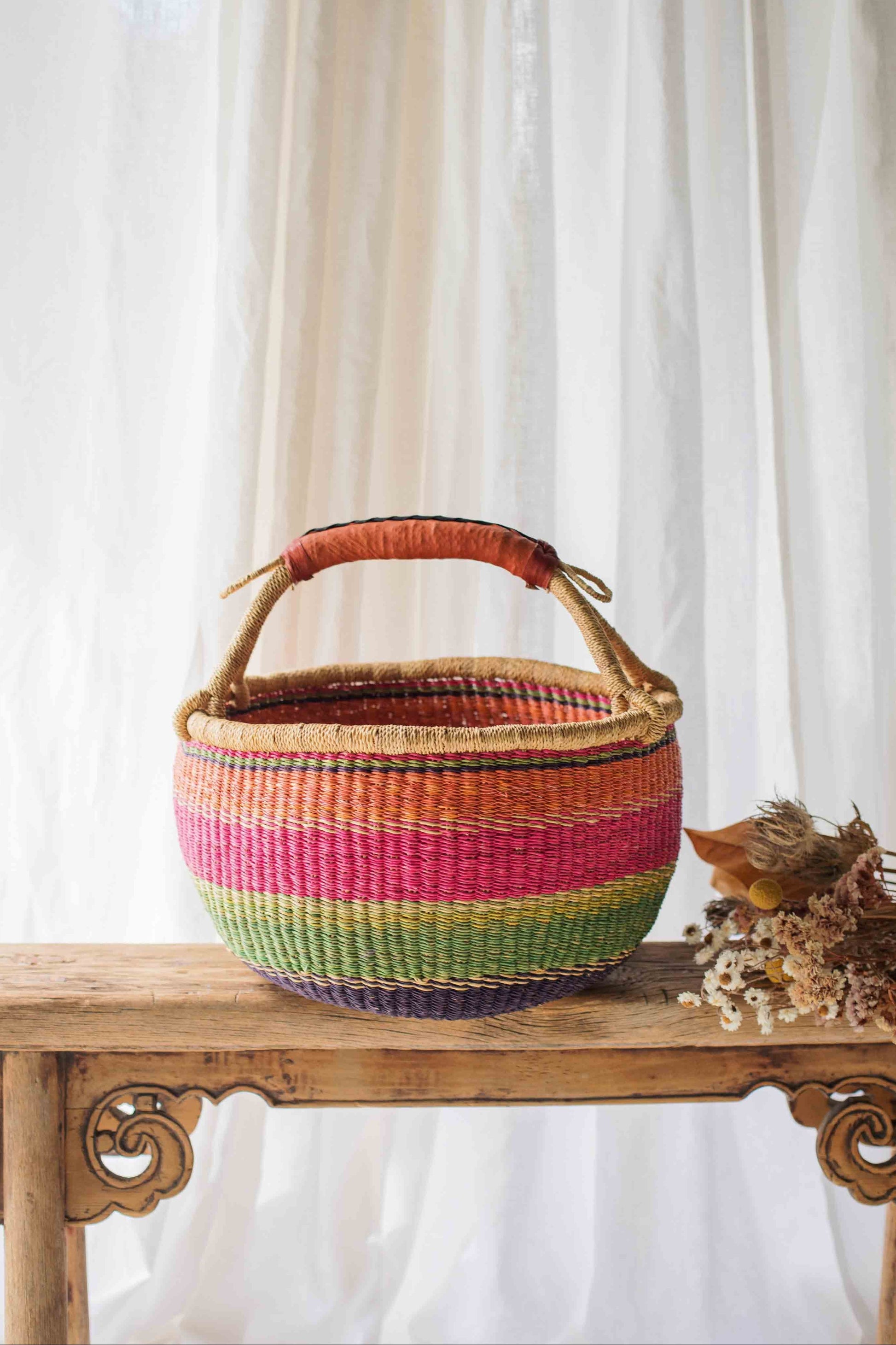 Colorful woven basket on a wooden table with a white curtain background