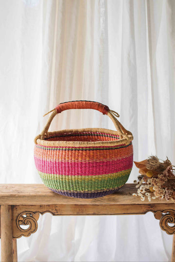Colorful woven basket on a wooden table with a white curtain background