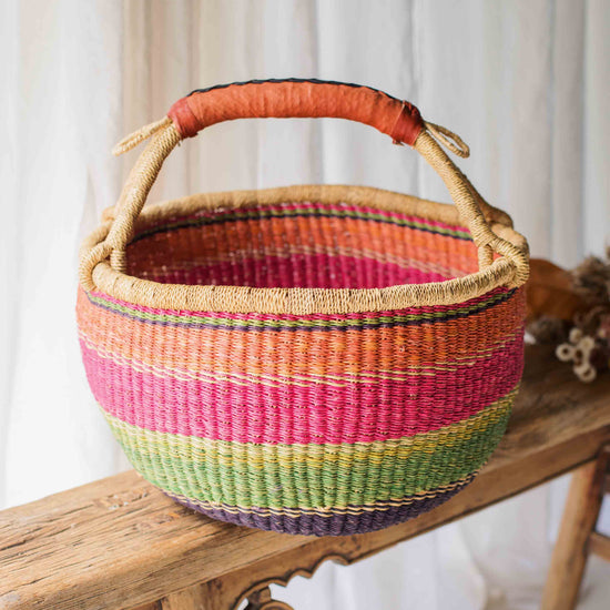 Colorful woven basket with a handle on a wooden bench against a white curtain background