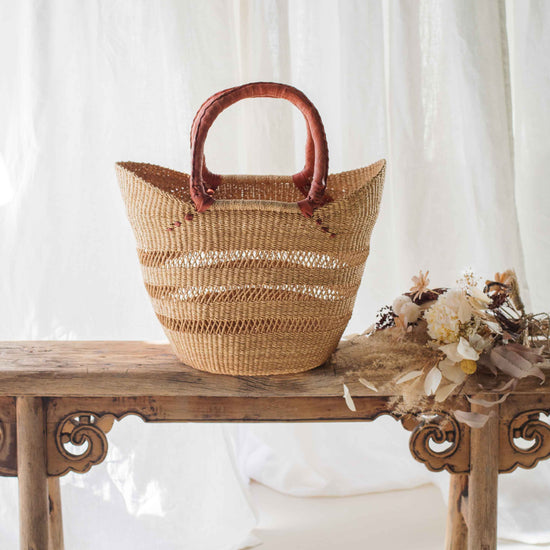 Woven basket with wooden handle on a wooden bench against a white curtain background