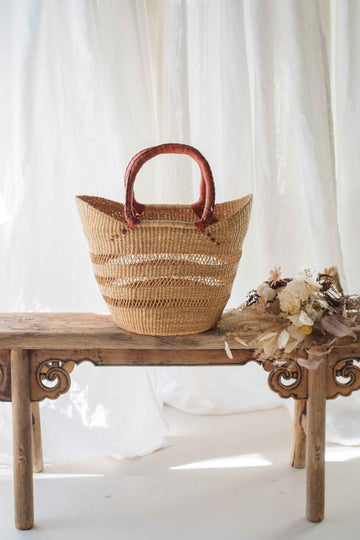 Woven basket with wooden handle on a wooden bench against a white curtain background