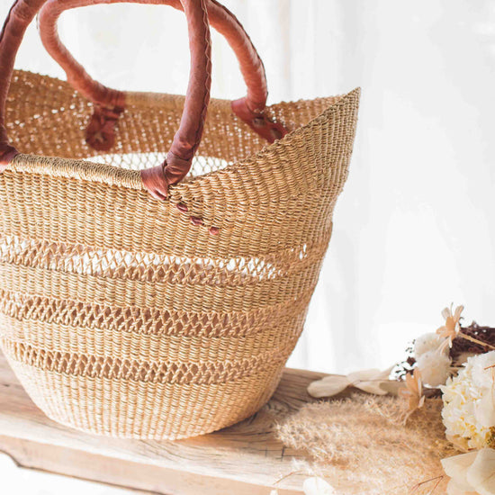 Woven straw bag with wooden handles on a white surface with flowers.