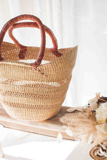 Woven straw bag with wooden handles on a white surface with flowers.