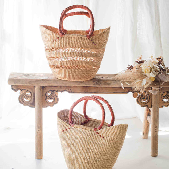 Two woven baskets with red handles on a wooden table against a white curtain background.