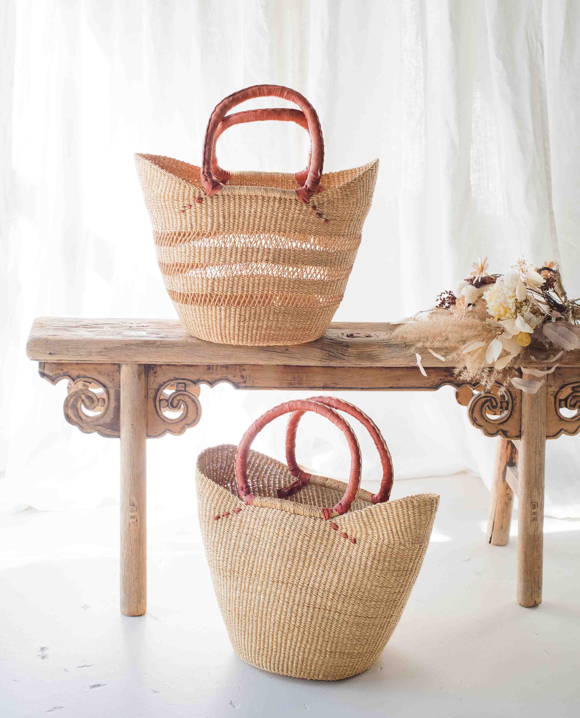 Two woven baskets with red handles on a wooden table against a white curtain background.