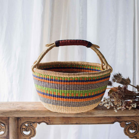 Woven basket with colorful stripes on a wooden table against a white curtain background