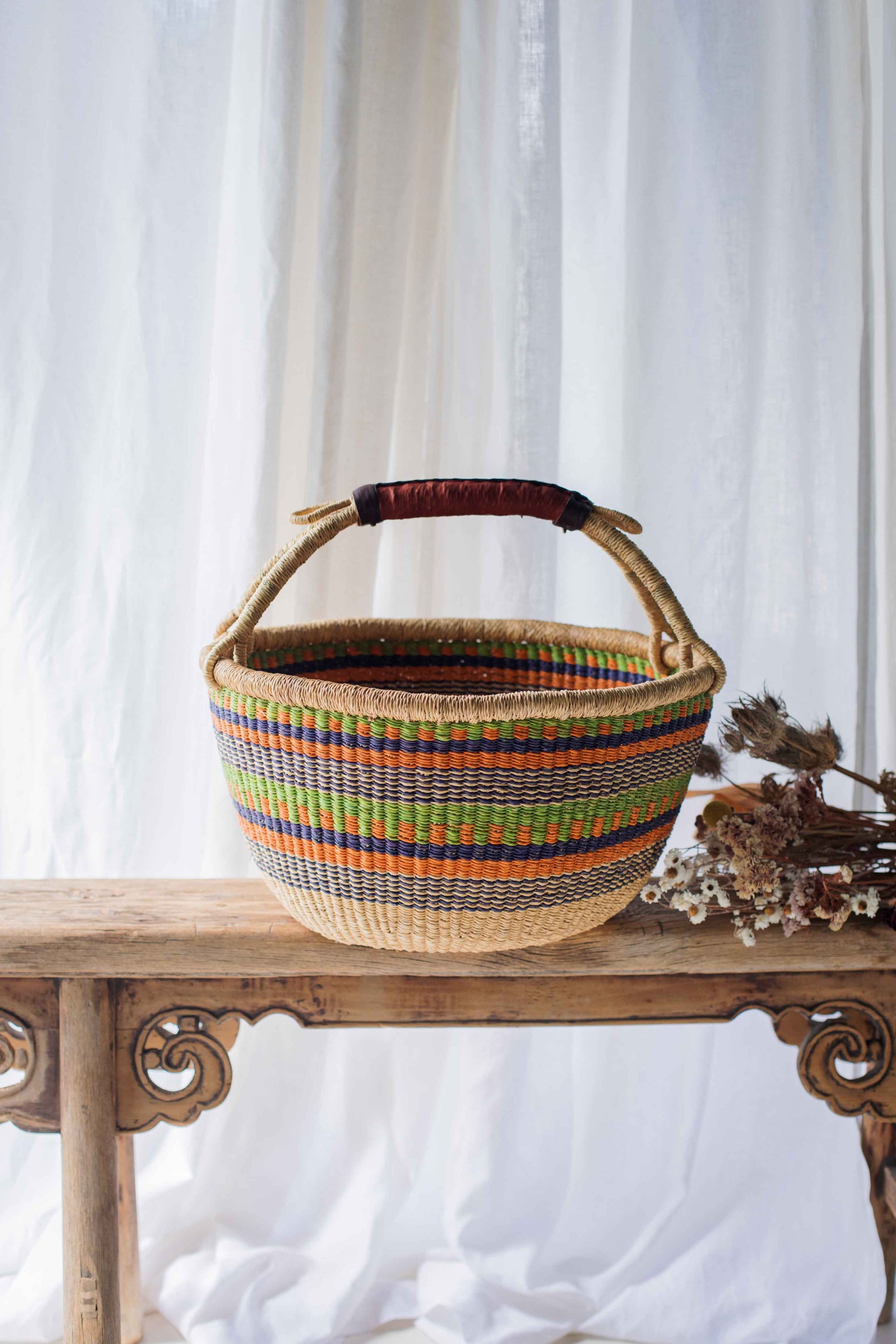 Woven basket with colorful stripes on a wooden table against a white curtain background