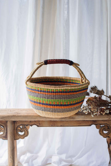 Woven basket with colorful stripes on a wooden table against a white curtain background