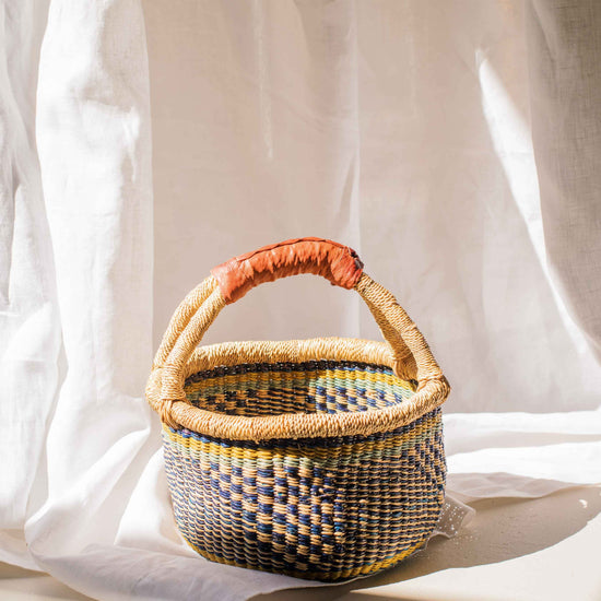 Woven basket with a red handle on a white fabric background