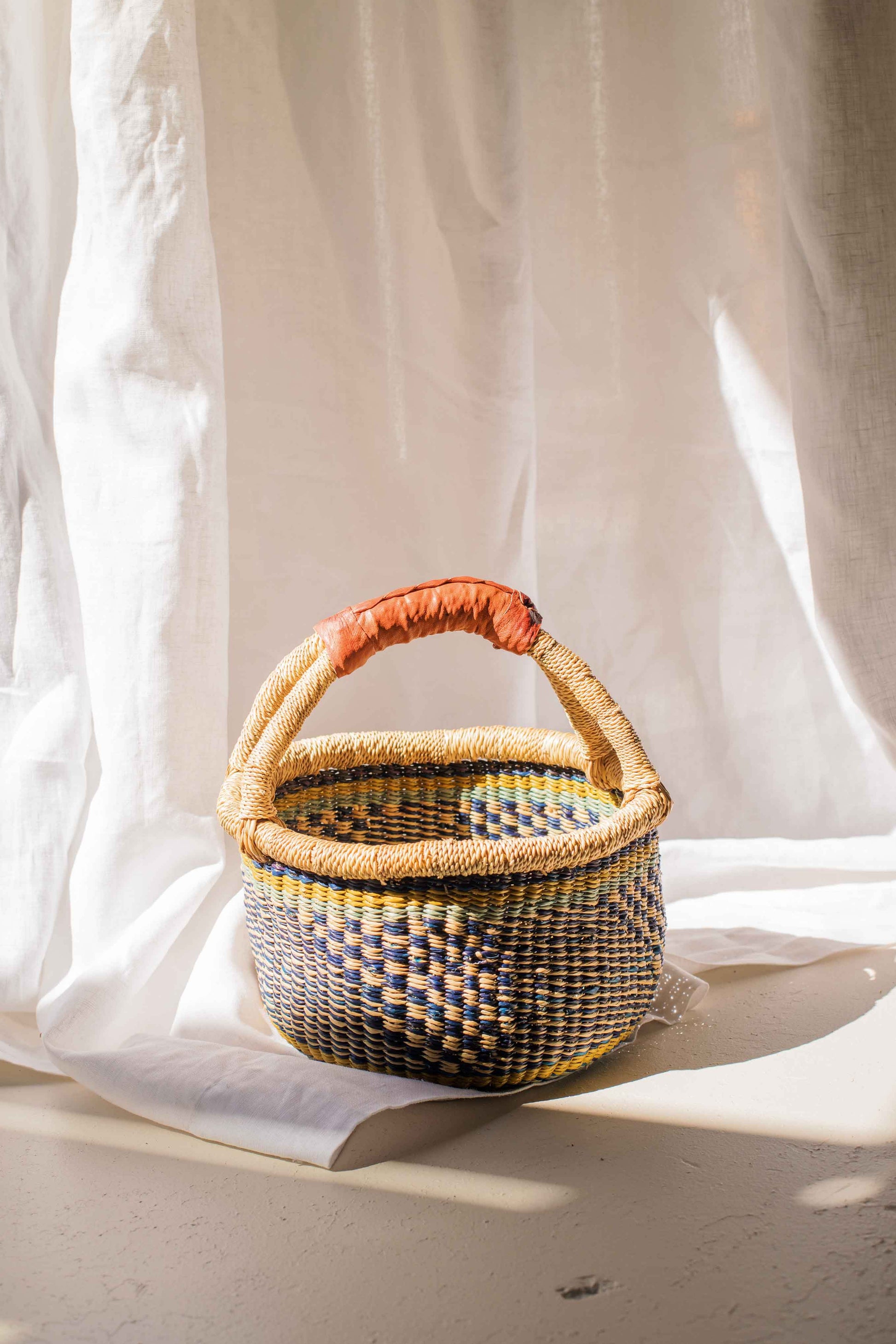 Woven basket with a red handle on a white fabric background