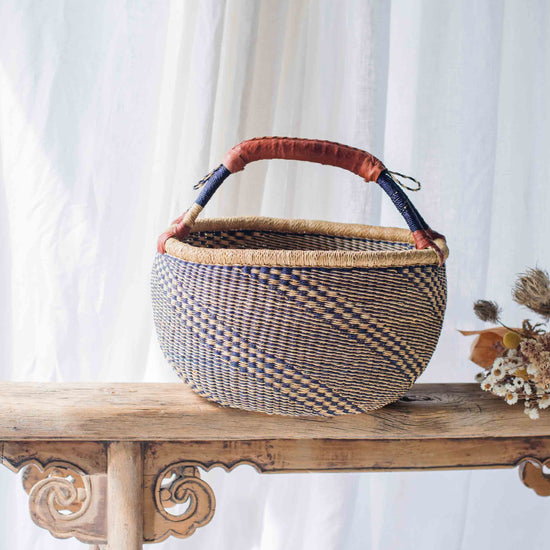 Woven basket with a checkered pattern on a wooden table against a white curtain background