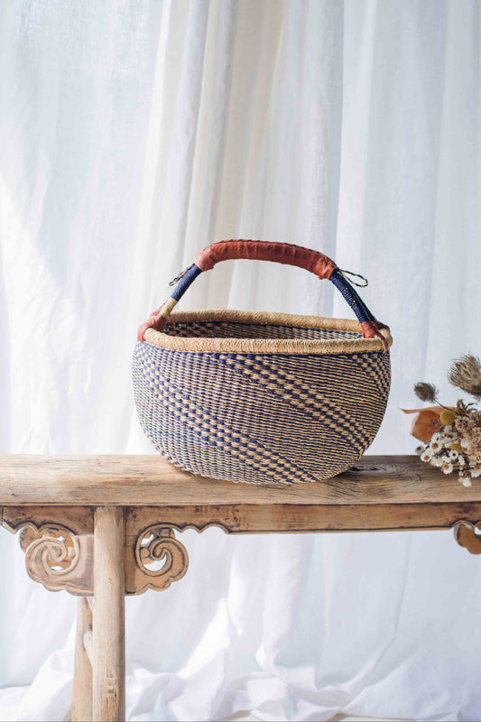 Woven basket with a checkered pattern on a wooden table against a white curtain background