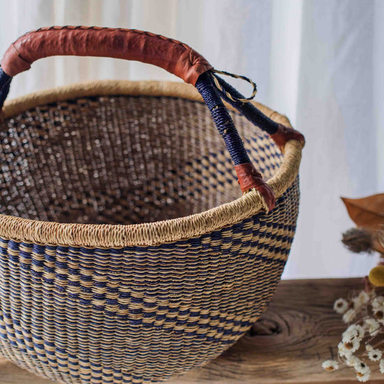 Woven basket with a red handle on a wooden surface with a white curtain background