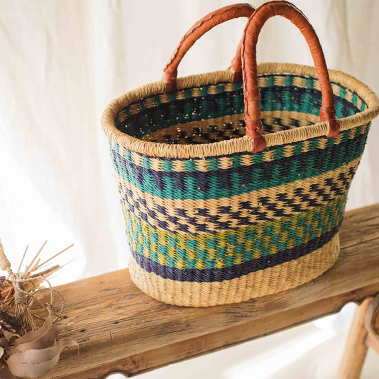 Woven basket with brown handles on a wooden surface against a white curtain background
