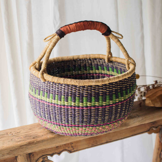 Woven basket with a handle on a wooden bench against a white curtain background