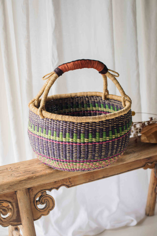 Woven basket with a handle on a wooden bench against a white curtain background