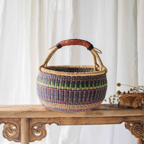 Woven basket with colorful patterns on a wooden table against a white curtain background