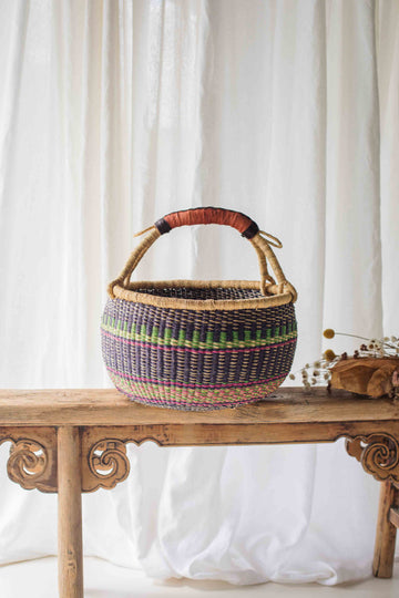 Woven basket with colorful patterns on a wooden table against a white curtain background