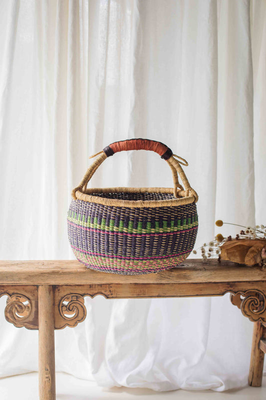 Woven basket with colorful patterns on a wooden table against a white curtain background