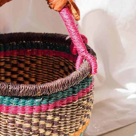 Woven basket with colorful handle on a white fabric background