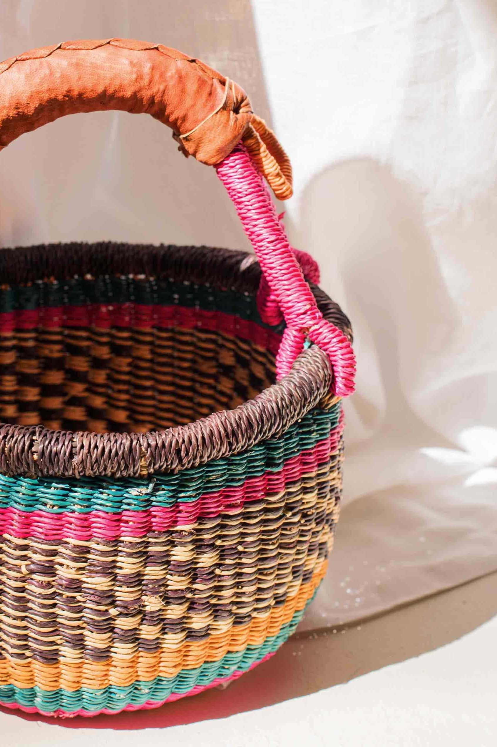 Woven basket with colorful handle on a white fabric background