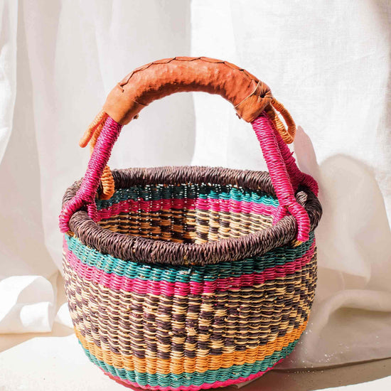 Woven basket with colorful handles on a white fabric background