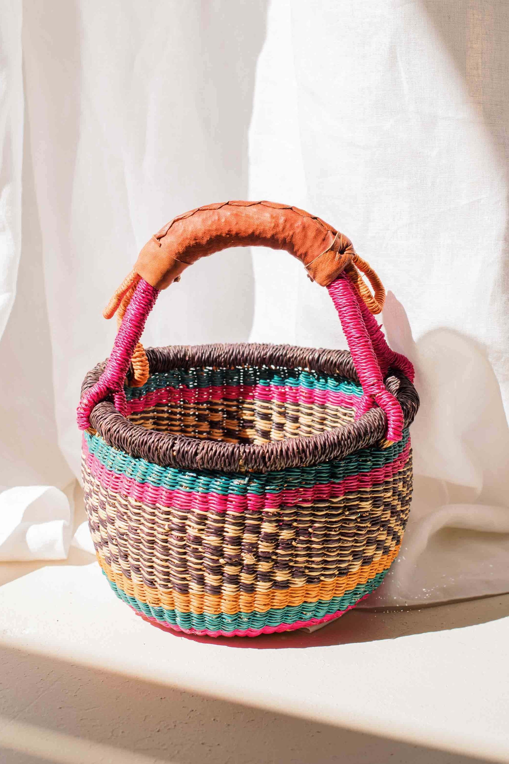 Woven basket with colorful handles on a white fabric background