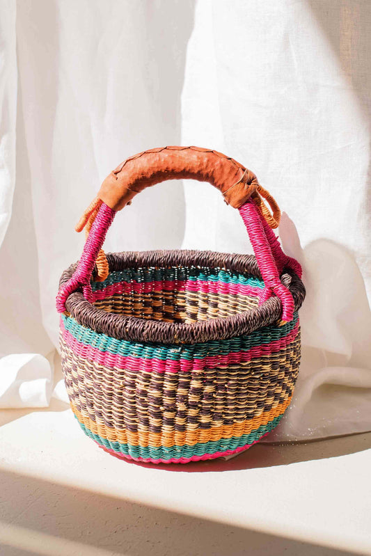 Woven basket with colorful handles on a white fabric background