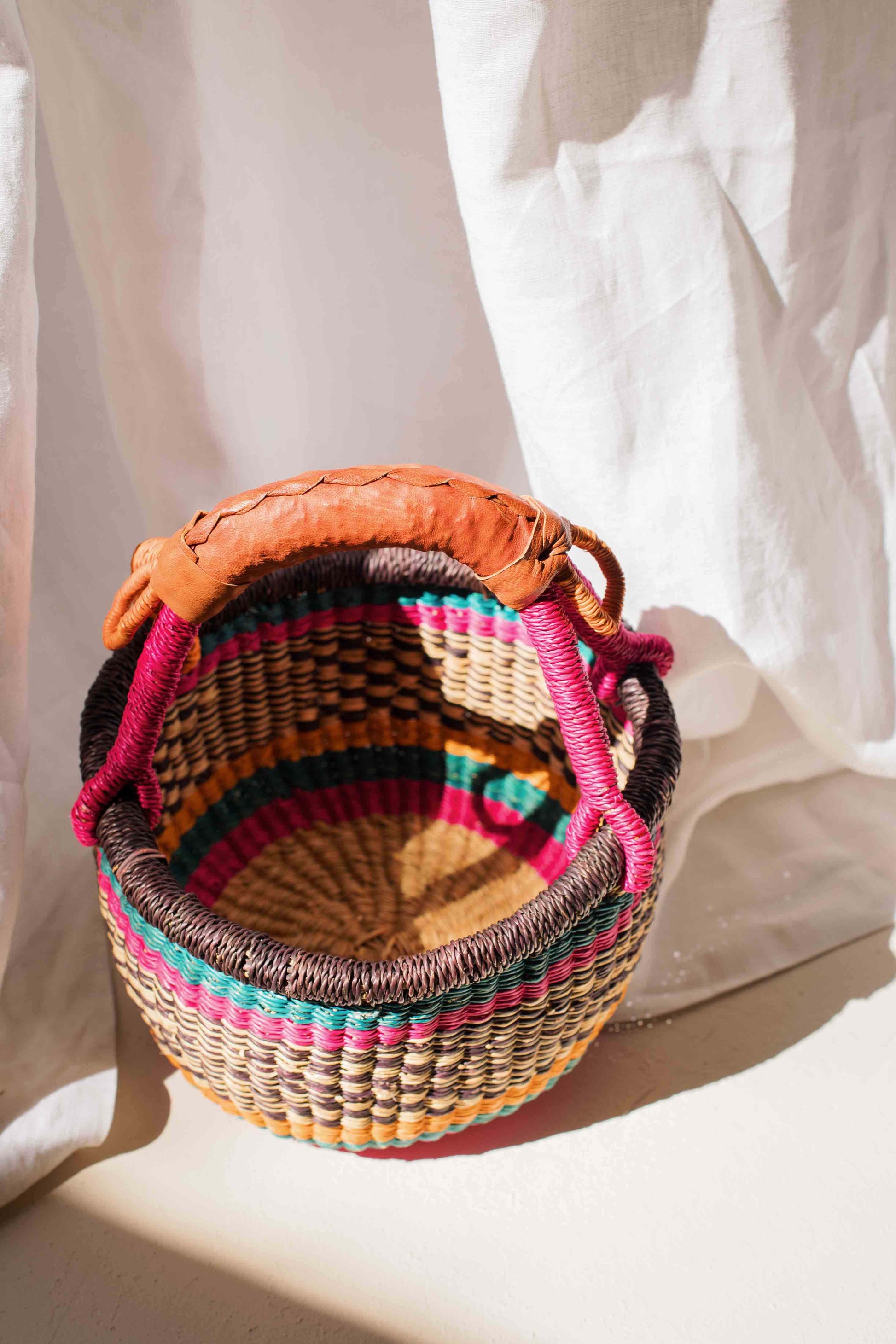 Multicolored woven basket with a brown lid on a white background