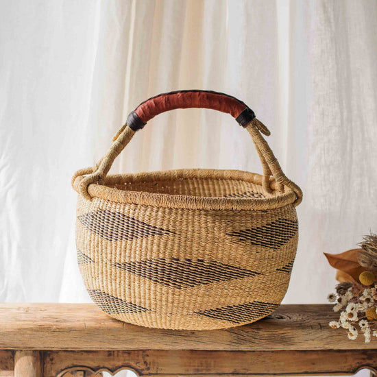 Woven basket with a red handle on a wooden table against a white curtain background