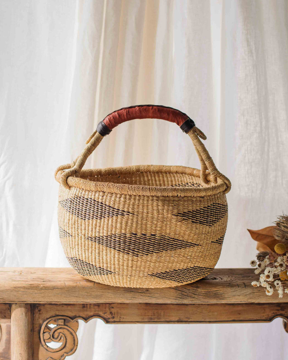 Woven basket with a red handle on a wooden table against a white curtain background
