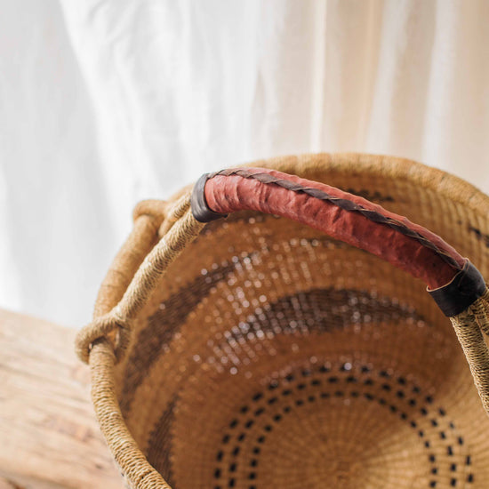 Woven basket with a red handle on a light wooden surface